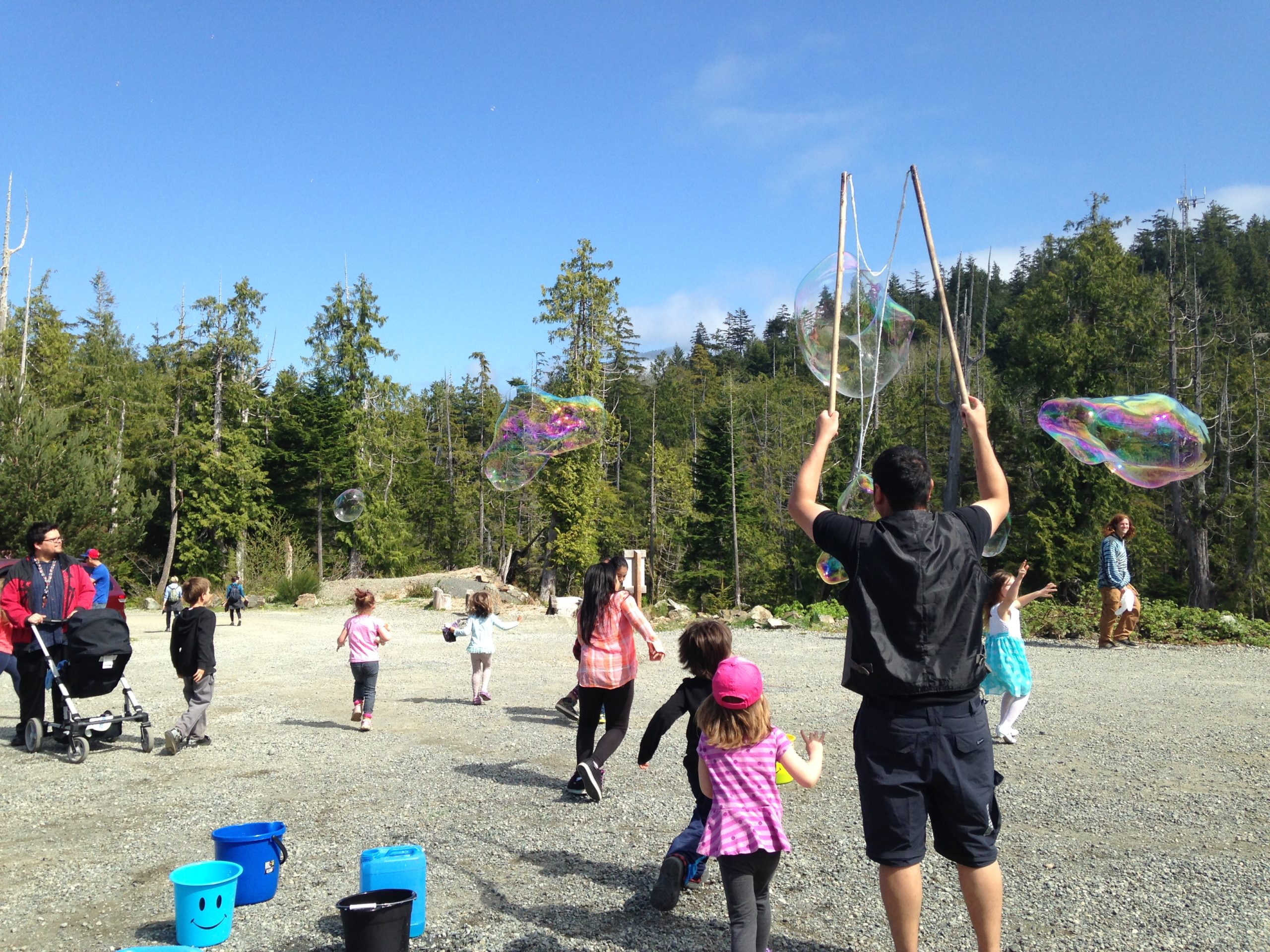NSG Project - Clayoquot Sound. A man making large bubbles on a beach with kids running around.